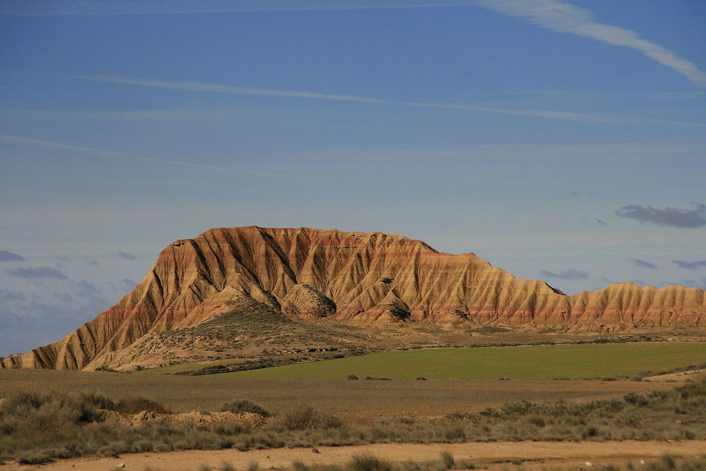 Cabezo de las Bardenas Reales con campos verdes a sus pies en un día despejado de otoño