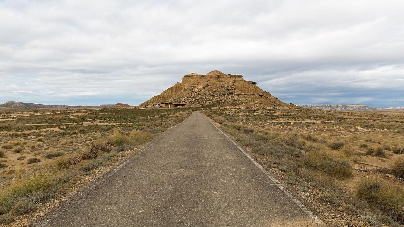 Straight track towards a butte in the Bardenas Reales, under a cloudy sky